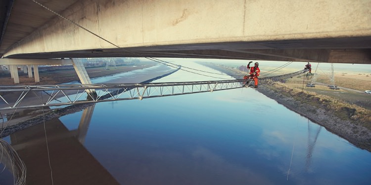 Workers on a beam under a bridge